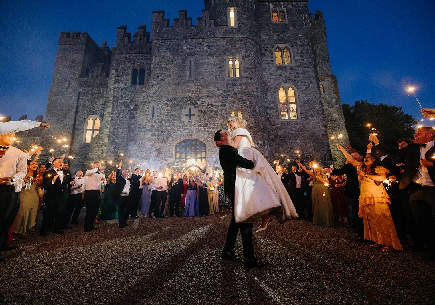 Wedding couple and guests with sparklers outside Kilkea Castle at dusk